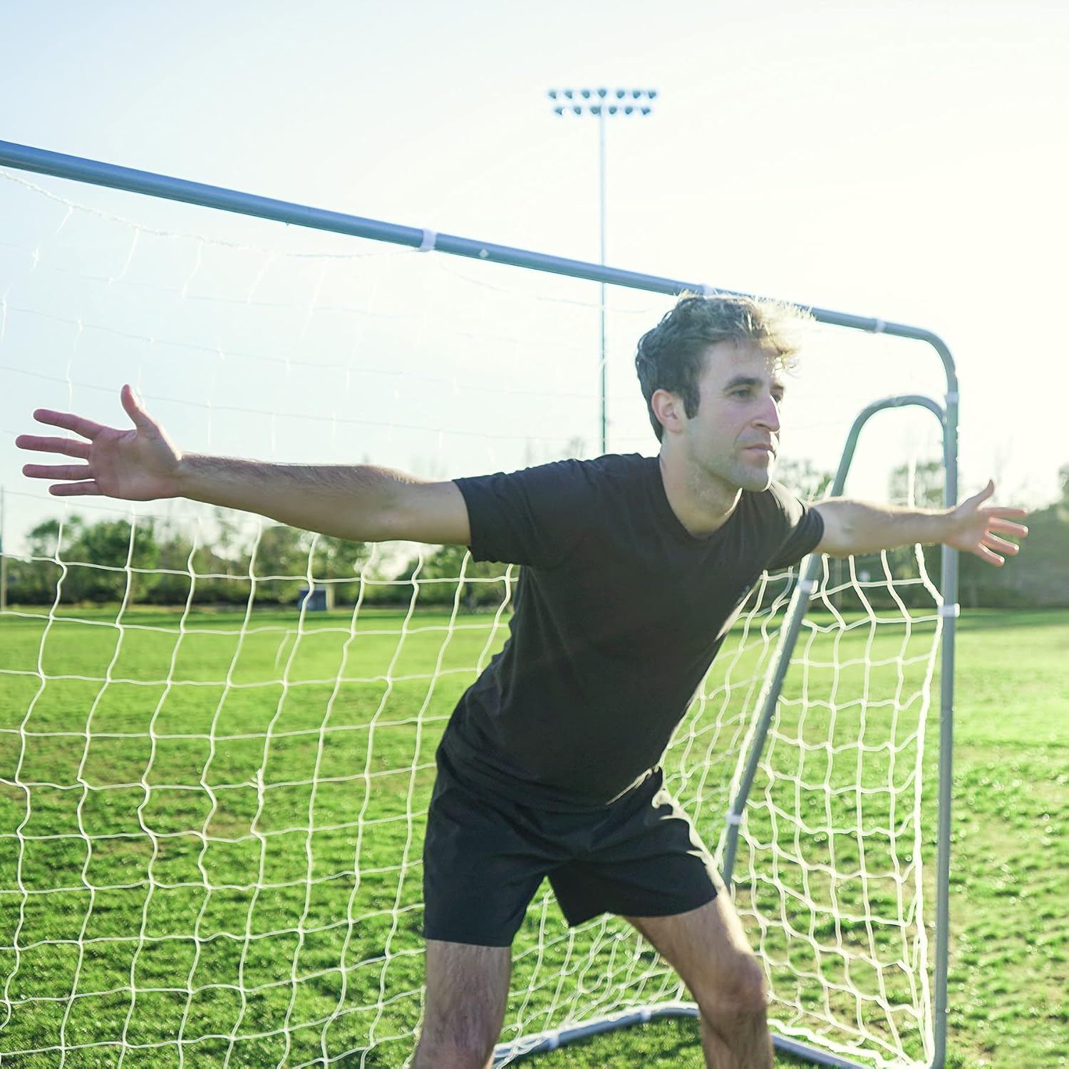 Man standing in front of a soccer goal on a grassy field