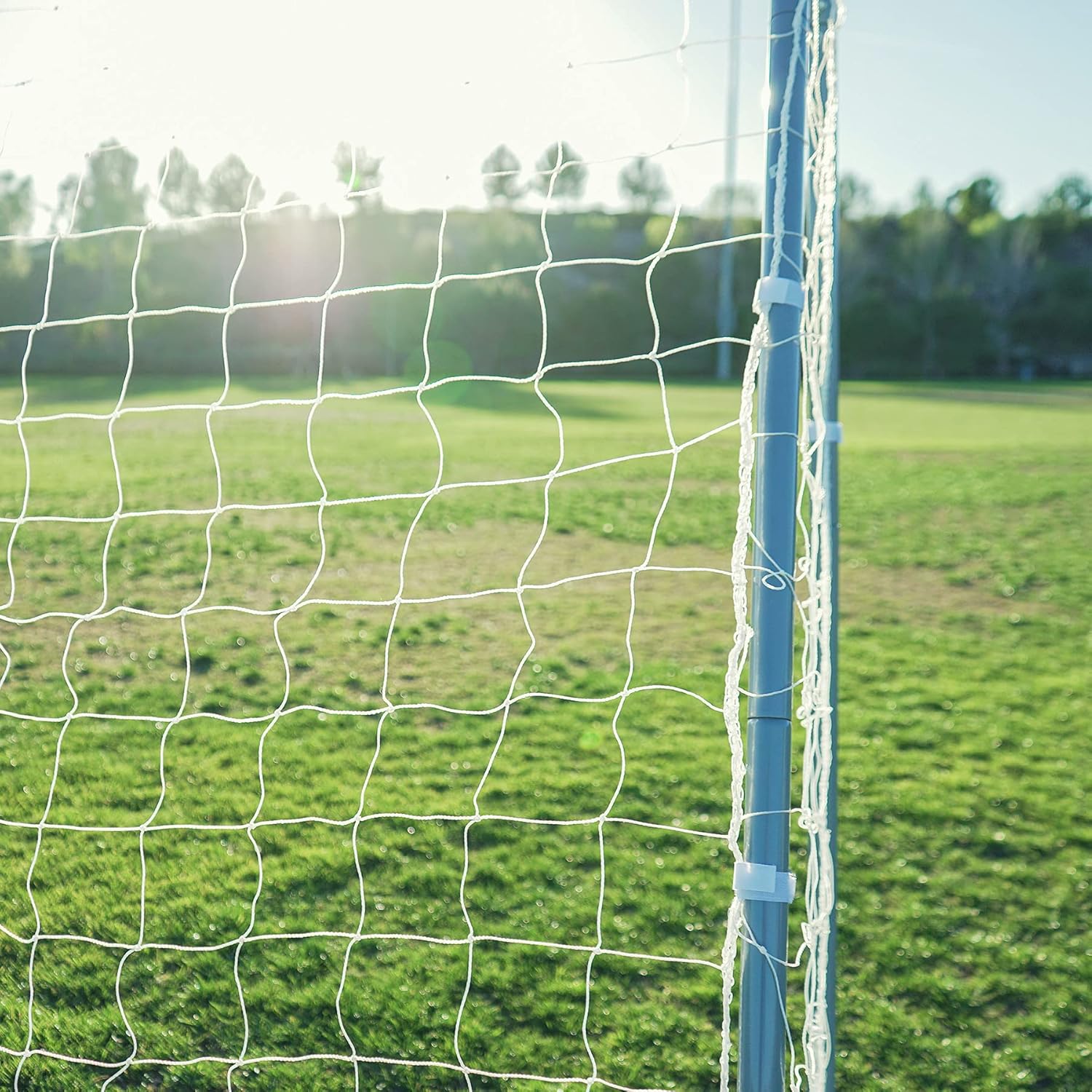 Soccer goal net on a grass field with trees in the background