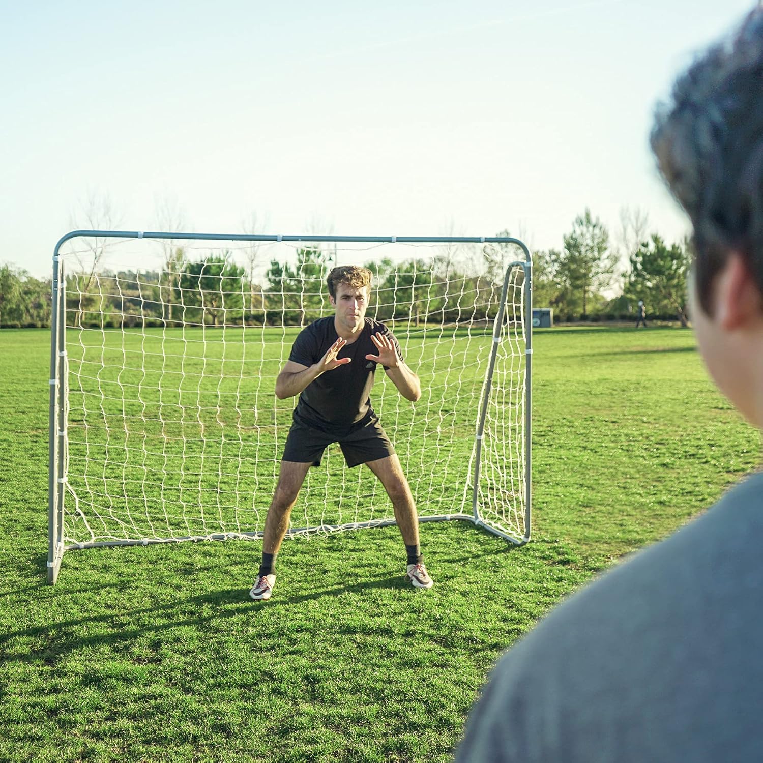 Person practicing soccer goalkeeping in a field with a goalpost.
